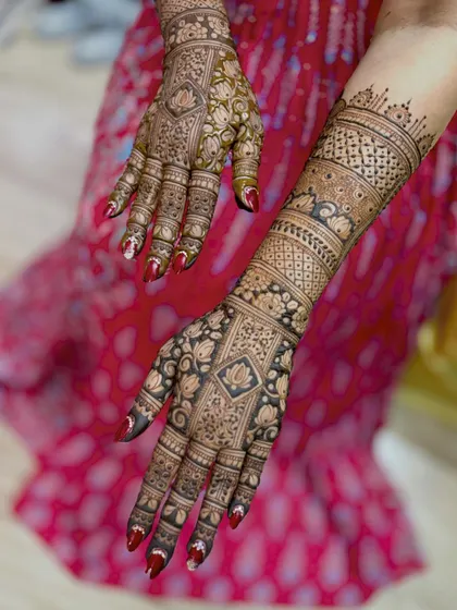 An intricate design with a mix of lotus motifs and geometric patterns, showing the fresh, dark henna paste.