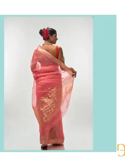 The back view of the salmon organza saree highlights the rich, floral gold zari work on the pallu, contrasting beautifully with the delicate buttis on the body.
