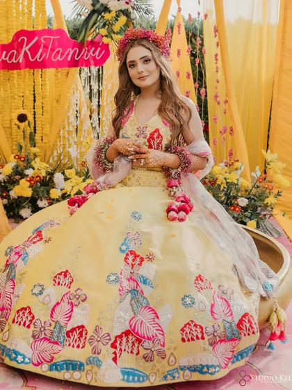 A beautiful portrait of the bride at her Haldi, seated in a large brass vessel, surrounded by yellow flowers.