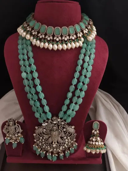 This pastel green Victorian set features a choker with pearl drops and a long necklace with a Krishna pendant. It's a beautiful choice for receptions or sangeet events.