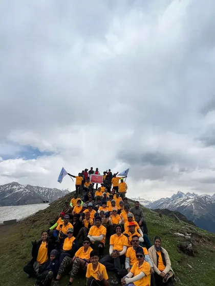 A group of trekkers at the summit of Chandrakhani Pass, with a panoramic view of the snow-capped peaks behind them.