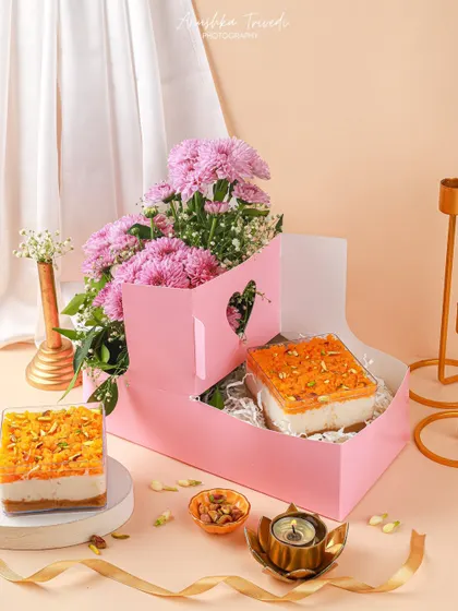 A beautiful pink Diwali hamper featuring a dessert box and fresh flowers, styled with elegant candle holders.