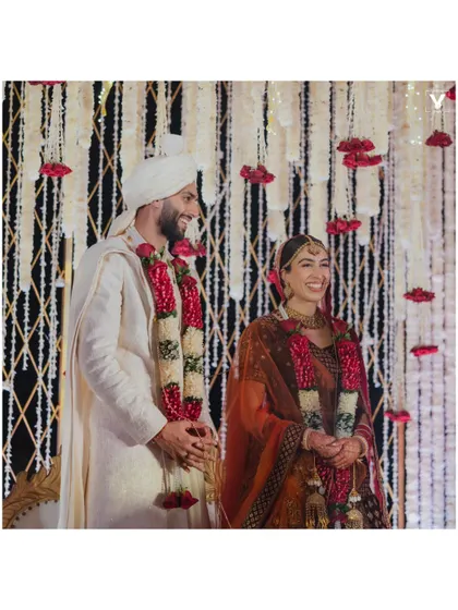 A classic portrait of the happy couple during their wedding ceremony. The backdrop of cascading white flowers with pops of red roses was designed to be both elegant and striking, perfect for timeless wedding photography.