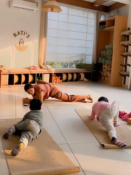An instructor helps a young student with a lizard pose, providing gentle encouragement and support.