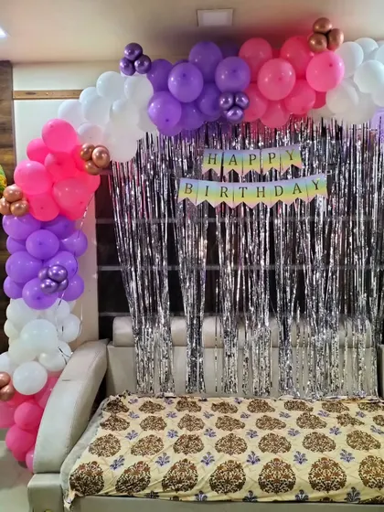 A colorful balloon half-arch over a sofa with a silver fringe curtain, an easy way to create a festive photo spot at home.
