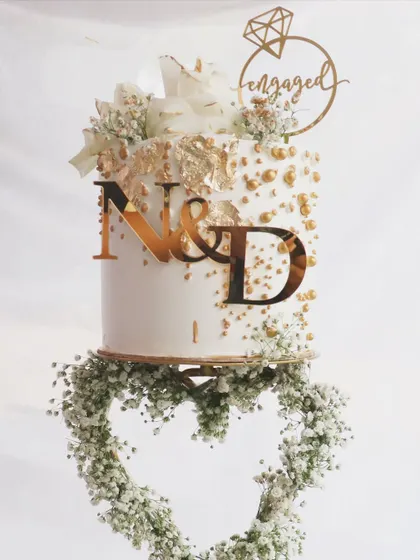A detailed shot of the top tier of this engagement cake, showing the 'Engaged' topper, gold leaf, and delicate baby's breath.