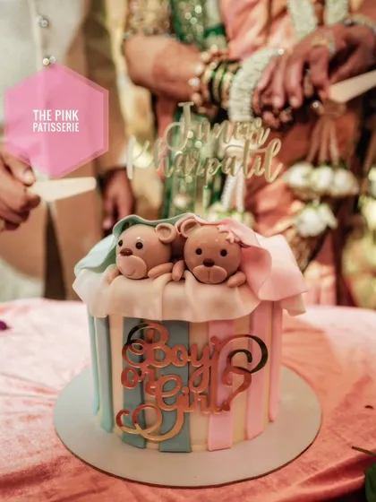 A "Boy or Girl?" gender reveal cake with pink and blue vertical stripes. The cake is topped with two cute fondant teddy bears under a blanket, adding to the sweet suspense.