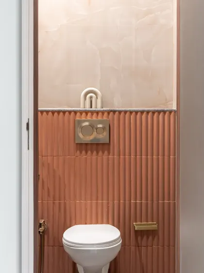 This powder room makes a statement with texture and color. The combination of fluted terracotta tiles and soft pink marble, accented with brass fixtures, creates a space that is bold, warm, and luxurious.