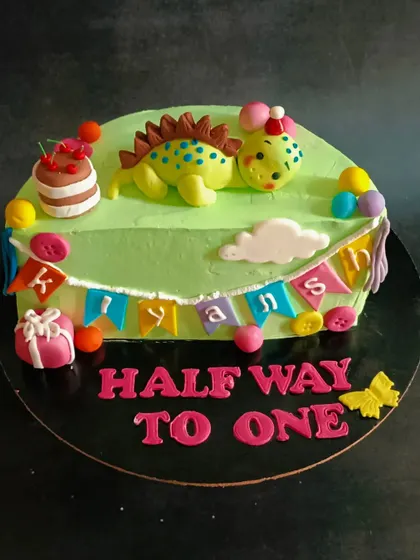 A cute dinosaur-themed cake celebrating a baby's half-birthday, marking the "halfway to one" milestone.