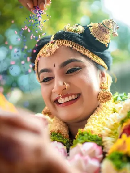 A close up of a bride's happy face as she's showered with flower petals during a wedding ritual. We capture the joy of these celebratory moments.