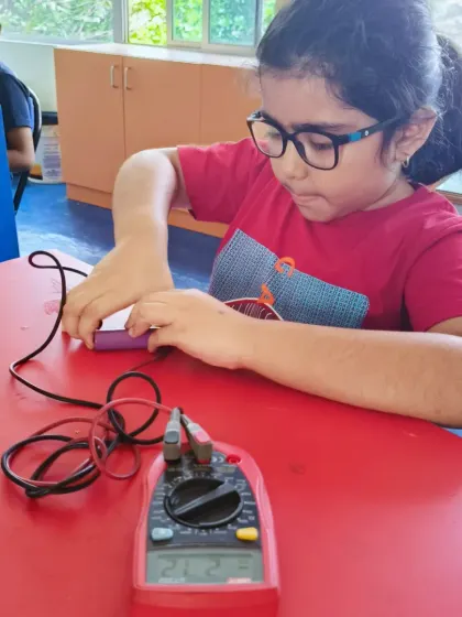 A young student learns to use a multimeter to test a battery. This teaches them about voltage and how to diagnose issues in their electronics projects, an essential skill for any budding engineer.