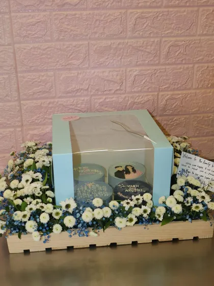 The complete engagement gift hamper, featuring our set of four personalized bento cakes nestled in a bed of fresh white and blue flowers. A beautiful way to welcome someone to the family.