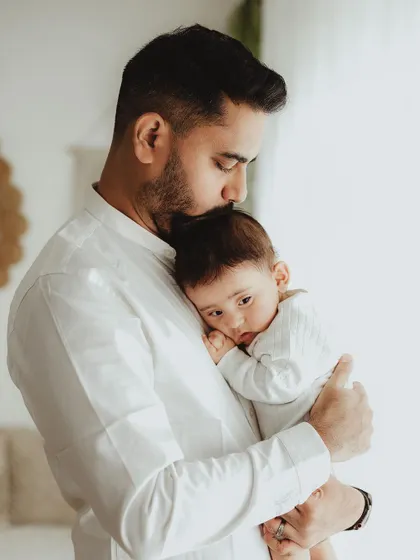 A father's gentle embrace. He kisses his baby's head while holding him close, a quiet and powerful portrait of paternal love.