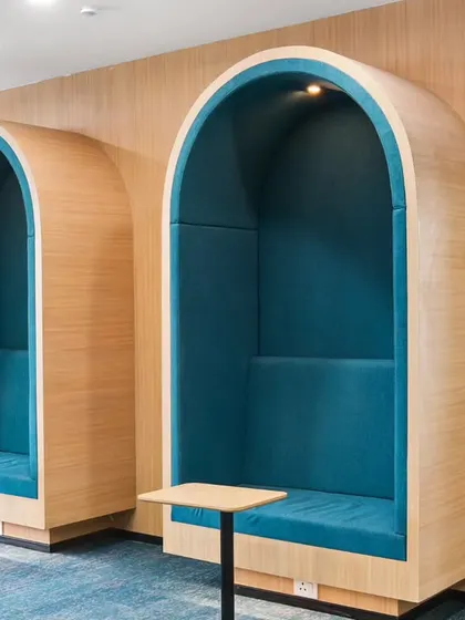 Modern acoustic phone booths in the office, providing private spaces for calls and focused work. The curved design and bold teal upholstery add a stylish and functional element to the open-plan workspace.