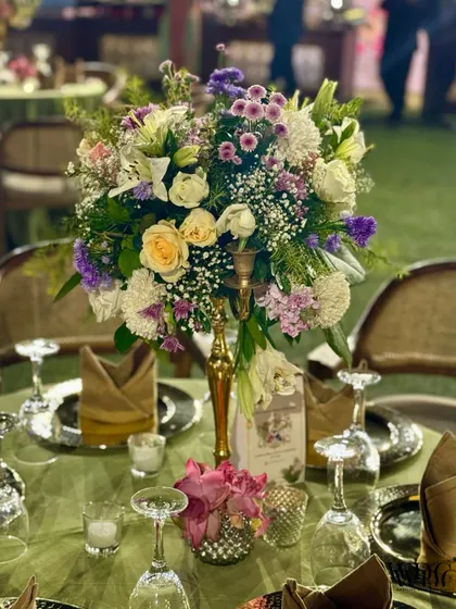 A detailed shot of the lush floral centerpiece, featuring a mix of white, yellow, and purple flowers in a golden vase.