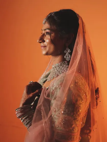 A side profile of the bride, with the soft light catching the delicate fabric of her pink dupatta and her diamond jewelry. This is a simple yet elegant bridal portrait.