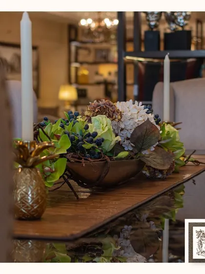 This centerpiece, featuring green and white hydrangeas and dark berries, sits elegantly on a wooden table runner, creating a natural and sophisticated tablescape.