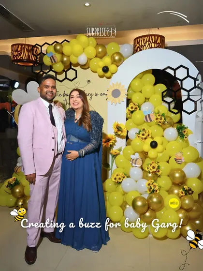 Creating a buzz for Baby Garg! The parents-to-be look so happy in front of the bee-themed baby shower backdrop I designed, complete with a honeycomb pattern and cheerful sunflowers.