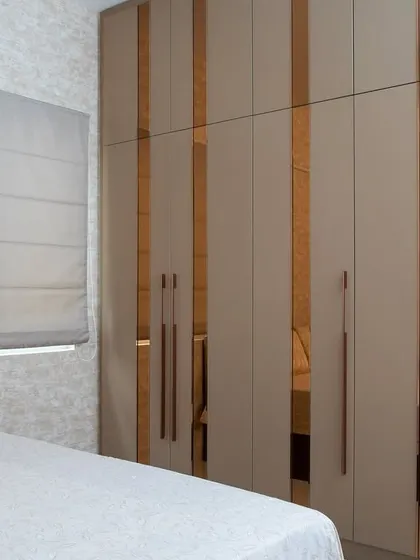 Here, I used beige laminate panels with vertical strips of rose-gold mirror. This detail not only adds a touch of glamour but also breaks up the solid surface and makes the wardrobe a standout feature in this neutral bedroom.
