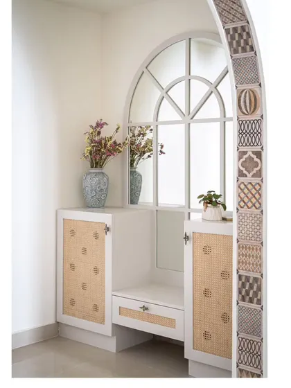 The foyer's shoe storage and seating unit, featuring a mirror that echoes the arch's shape. The design uses cane shutters and a clean white finish to create a bright and functional entryway.