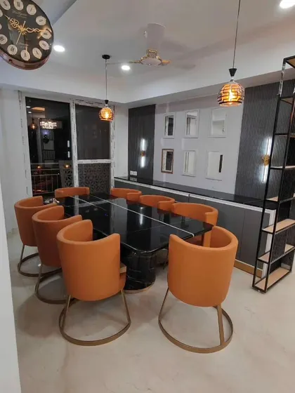 This dining space features a gallery of assorted small mirrors on the wall, creating a unique and artistic focal point above the sideboard. The orange chairs add a vibrant pop of color.