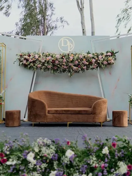A perfect example of modern minimalist design for an engagement stage. The clean, curved backdrop is accented with geometric gold frames and asymmetrical floral arrangements, creating a chic and sophisticated look.