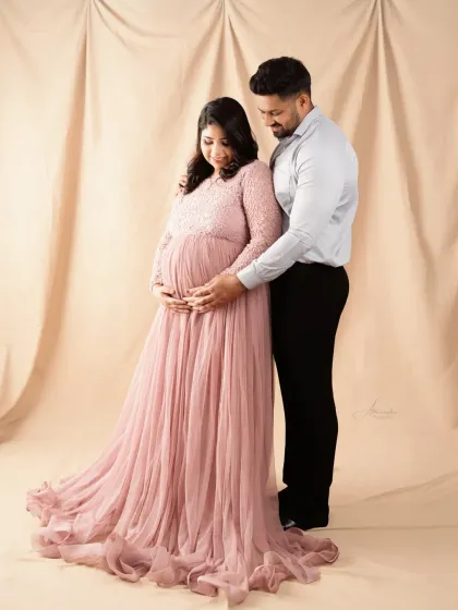 A classic couple's pose, with the dad-to-be gently holding the baby bump. The soft pink lace gown adds a touch of romance to this beautiful memory.