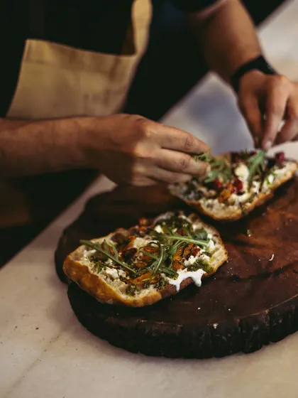 A chef carefully places fresh arugula on top of the Stracciatella Bruschetta. This final touch adds a peppery bite that balances the richness of the cheese.