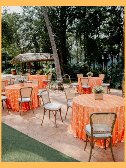 Casual outdoor seating for a Haldi, with bright orange patterned tablecloths adding a splash of color to the natural surroundings.