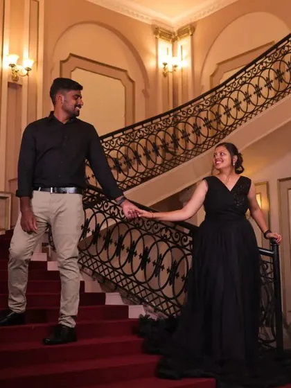A couple descends a grand staircase hand in hand. The client's black gown with a sheer trail adds a touch of classic elegance.