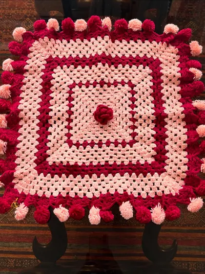 A full view of the pink and red pompom tablecloth, showcasing its square shape and central rosette detail.