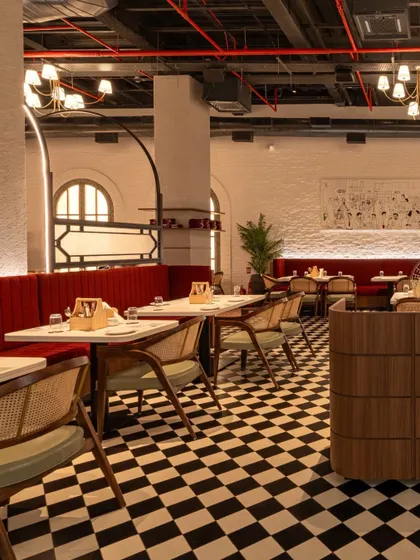 This view shows the interplay of textures, from the painted brick wall and checkerboard floor to the plush red velvet of the booths and the warm wood of the chairs.
