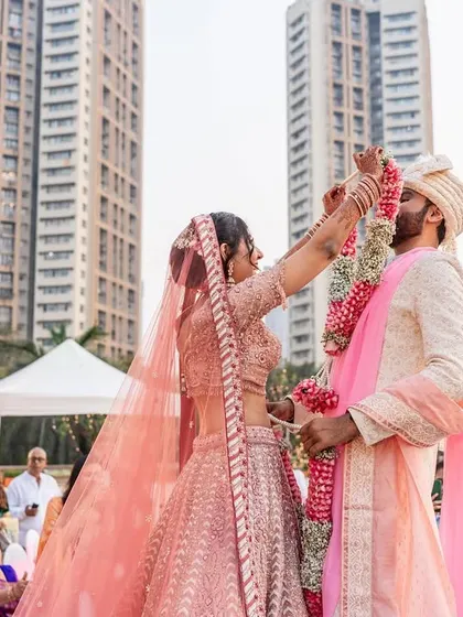 The bride reaches up to place the garland on the groom, a classic moment of playful challenge during the varmala ceremony.