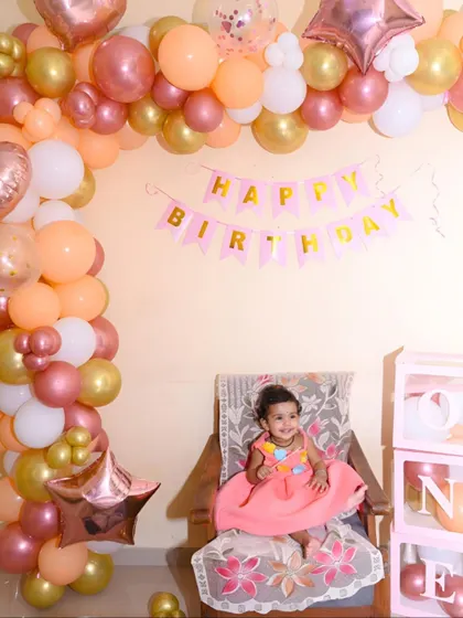 The birthday girl seated like a princess in her chair, surrounded by a beautiful arch of pastel balloons.