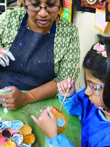 An instructor helping a young student with her clay painting project. Our classes for the 8-13 age group involve a wide range of mediums to keep them engaged and learning.