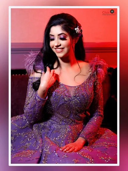 An indoor portrait with dramatic, colorful lighting. The model's joyful expression is highlighted by the warm red and purple tones, showcasing our ability to create glamorous, high-fashion looks for evening events or engagement parties.