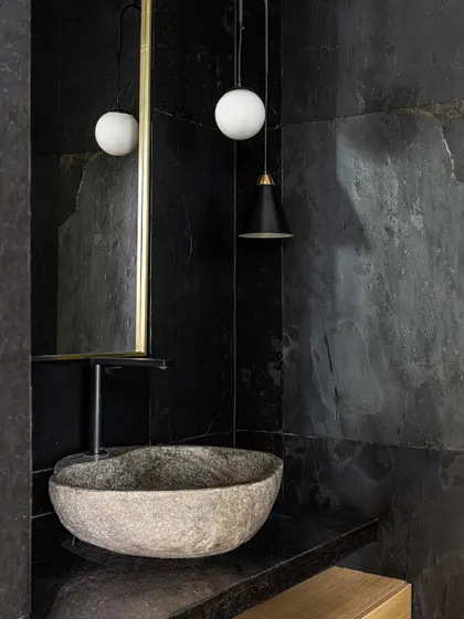 This moody, monochrome powder room features walls clad in black slate tiles and a rustic stone sink. The design is minimal yet powerful.