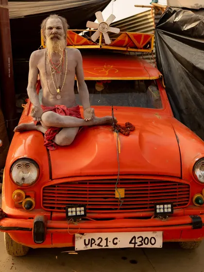 Ambassador Baba sits in meditation on the hood of his iconic orange Ambassador car at the Kumbh Mela. It's a unique blend of modern machinery and ancient asceticism.