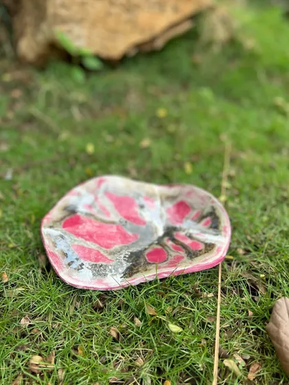 A stoneware wall piece with a striking pink and black abstract design. While it can be hung on a wall, it could also serve as a unique decorative platter on a coffee table.
