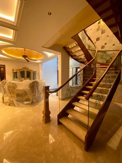 This open-plan living and dining area is defined by its grand, curving staircase. Crafted from wood with glass railings, it acts as a functional sculpture, adding a sense of luxury and openness to this Bengaluru duplex.