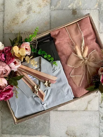 Engagement trousseau packaging for a client. This tray features elegantly packed outfits for the groom, adorned with a stunning arrangement of pink and burgundy flowers.