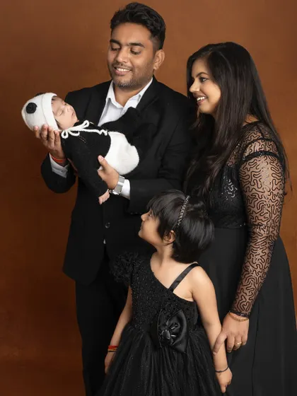 The family of four complete. The father proudly holds his newborn while the mother and big sister look on with adoration in this classic family photo.