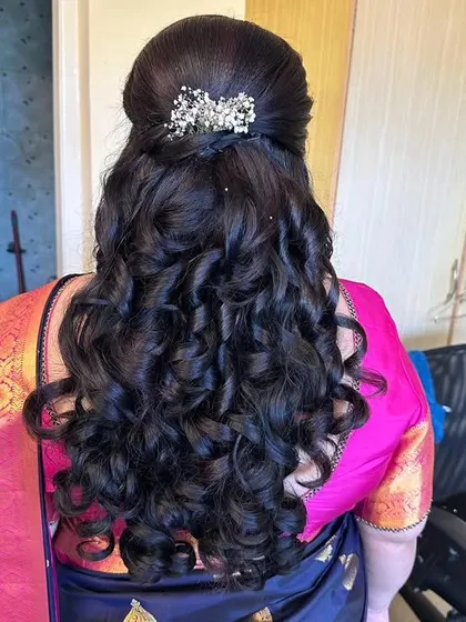 A half-up style with a small braid and tight curls, accented with a delicate, sparkling clip.