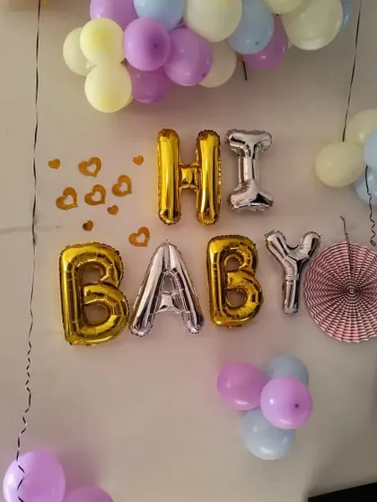 Even simple home decorations can be special. This "Hi Baby" setup uses gold and silver foil balloons, paper fans, and a pastel balloon garland for a sweet and easy baby welcome.