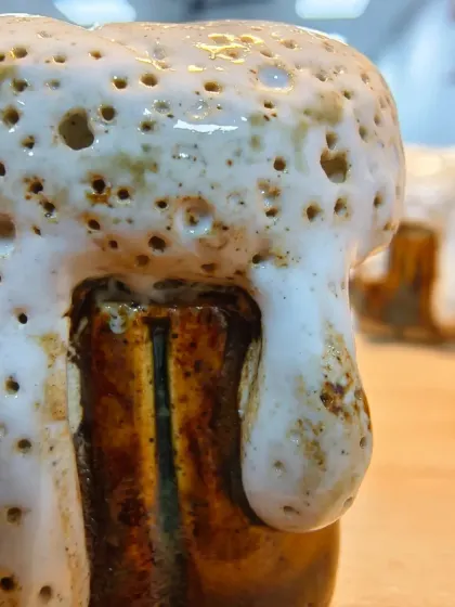A macro shot of a miniature ceramic beer mug, complete with a frothy, textured glaze that looks just like foam. This is a perfect example of creative glazing.