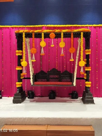 A classic wooden jhoola (swing) decorated with marigold flowers, set against a bright pink backdrop. This is a simple yet beautiful setup for a Haldi or Mehendi ceremony.