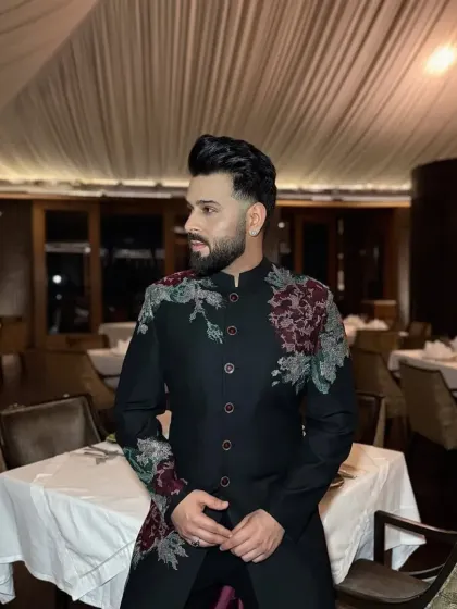 This black sherwani features large, artistic floral embroidery in maroon and grey threadwork on the shoulder and chest. It's a modern take on traditional motifs, designed for formal evening events.