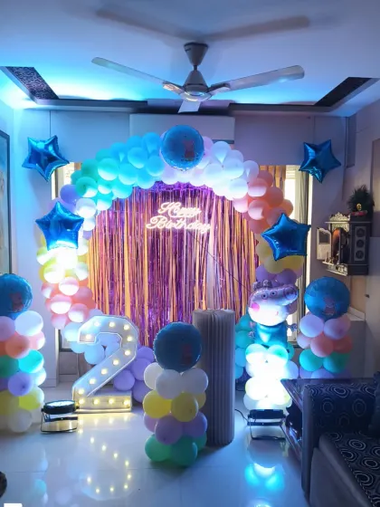A colorful balloon arch and columns set up in a living room. This decoration uses a tinsel curtain and a marquee number '2' to create a festive party space at home.