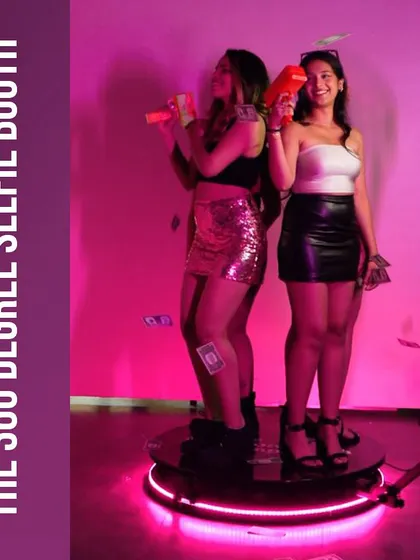 Two guests having a blast on the 360 Degree Selfie Booth platform, complete with fun props like money guns. We provide a variety of props to elevate the video experience.