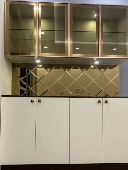 A beautiful crockery unit with bronze-tinted glass upper cabinets and a beveled mirror backsplash. The under-cabinet lighting highlights the display and adds a warm glow to the dining area.